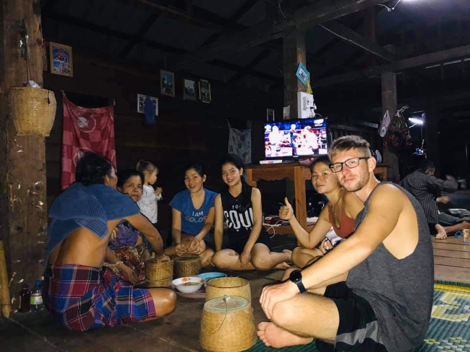 people sitting on the floor in a local wooden lao house and eating together